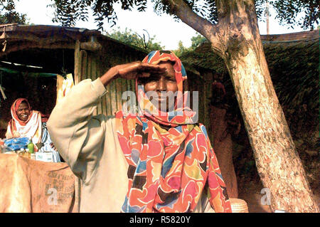 1993 - Straight on shot of a Somali woman from the waist up as she renders a salute to show her support for American Forces (not shown) in Somalia in support of Operation Continue Hope.  The photograph was taken in the market area of Kismayo, Somalia.  Another Somali woman is seen at the left in the background and she's laughing.