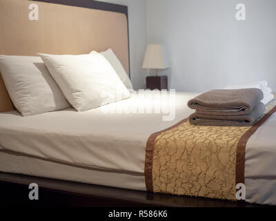 Clean towels and three white pillows on bed in luxury room in hotel. Stock Photo