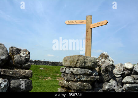 A sign atop a dry stone wall reading 'public footpath' indicating the direction of The Dales Way hiking trail in Yorkshire, England, United Kingdom Stock Photo