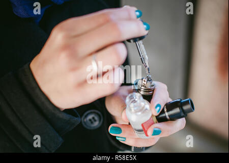 portrait of young beautiful woman with white hair, in a black coat, a skirt and a black hat, smoking an electronic cigarette, runs vape juice electronic cigarette. He holds a mechanical mod with RDA. Stock Photo