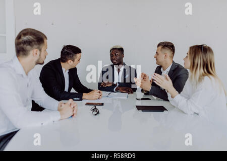 Multiracial business people applauding sitting at conference table, diverse team clapping hands after group meeting Stock Photo