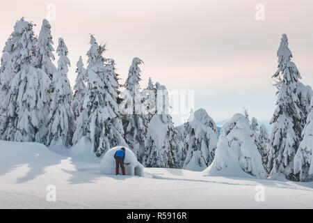 Man in blue jacket building igloo in the high mountain. Fantastic winter scene Stock Photo