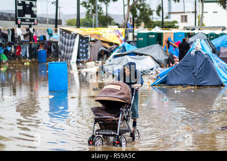 Tijuana, Mexico. 29th Nov, 2018. A young person pushes a pram through the flooded Benito Juarez sports complex, which serves as emergency shelter for migrants. More than 6000 Central American migrants on the US border move to larger accommodation. The previous migrant accommodation in a sports facility was only designed for 3000 people and was overcrowded. Credit: Alejandro Gutiérrez Mora/dpa/Alamy Live News Stock Photo