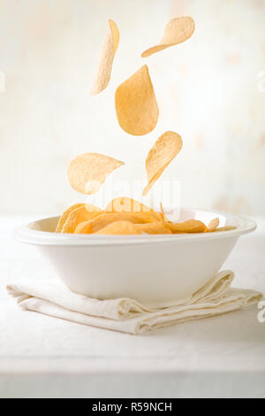 Potato Chips Falling in a White Bowl Stock Photo