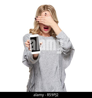 Portrait of shocked pretty blond woman covering her eyes with hand showing mobile phone blank screen isolated over white background. Shocking news, pr Stock Photo