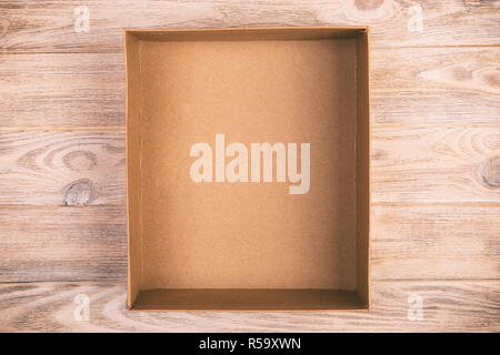 Opened cardboard box on wooden background. vintage, toned top view. Stock Photo