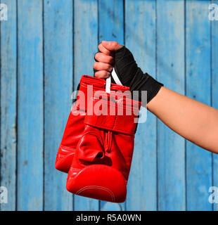 Red boxing gloves hanging on a rope in a woman's hand Stock Photo