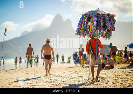 RIO DE JANEIRO - FEBRUARY, 2018: A Brazilian vendor selling bikinis carries his merchandise hanging from an umbrella along the shore of Ipanema Beach. Stock Photo
