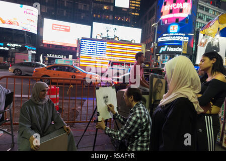 New York City, USA - July 30, 2018: Cartoonist doing a portrait in pencil to a Muslim girl with hijab on Times Square at night with people around and  Stock Photo