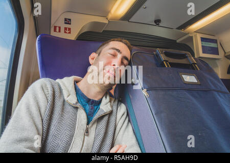 Young man traveling on a train and sleep on blue suitcase next to him Stock Photo