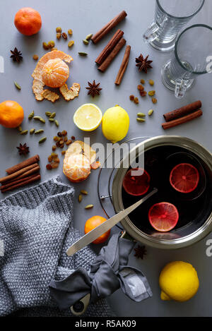 Mulled wine in aluminum casserole on gray wooden table. Christmas or winter warming drink. Ingredients: wine, lemon, cinnamon sticks, anise, cardamon, Stock Photo