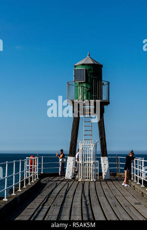 People standing under the Whitby West Pier Extension Starboard Green Beacon on Harbour Entrance Stock Photo