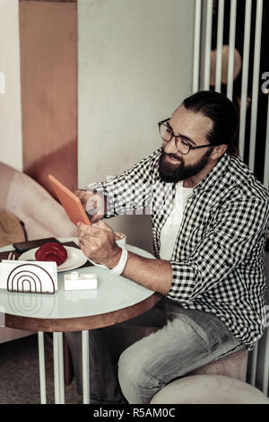 Modern gadget. Cheerful bearded man using his tablet while checking his social networks Stock Photo