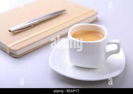 stylish notebook, ballpoint pen and white cup with a fragrant espresso coffee on the office desk Stock Photo
