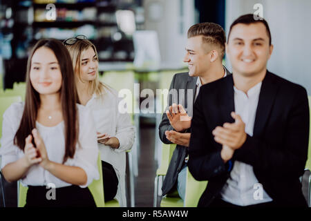 Multi ethnic business group greets somebody with clapping and smiling Stock Photo