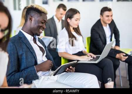 Multi-ethnic office people group using gadgets at team meeting, serious executives working on mobile phones during corporate briefing break, employees Stock Photo