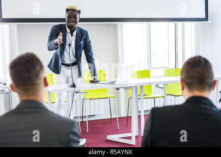 Young man raising hand to ask question, boss leader businessman presenting new project to multiracial millennial colleagues during briefing. Corporate Stock Photo
