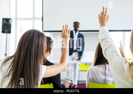 Young man raising hand to ask question, boss leader businessman presenting new project to multiracial millennial colleagues during briefing. Corporate Stock Photo