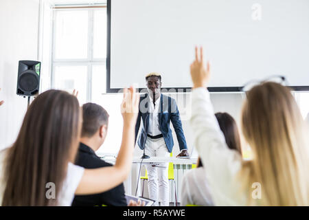 Young man raising hand to ask question, boss leader businessman presenting new project to multiracial millennial colleagues during briefing. Corporate Stock Photo