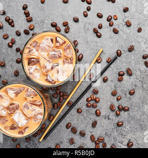 Cold brewed iced coffee in tall glass with coffee beans and straws on grey concrete background. Chocolate, vanilla, caramel or cinnamon iced coffee in Stock Photo
