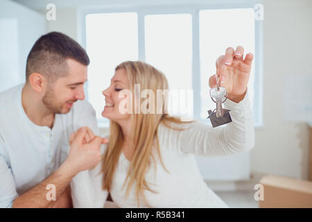 Young couple in love sitting inside of new apartment and showing keys excited with relocation Stock Photo