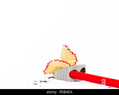 Close up view of a red pencil being sharpened in a metallic pencil sharpener with wood shavings around it. Stock Photo