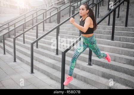 Picture of fast running model. She does it on steps. Young woman helps herself with hands. She runs as fast as she can. Young woman poses on camera in Stock Photo