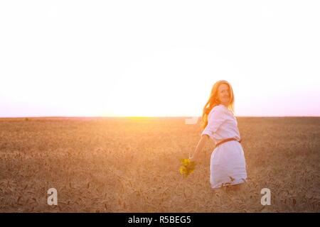 young girl joys on the wheat field at the sunset time Stock Photo