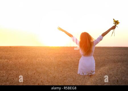 young girl joys on the wheat field at the sunset time Stock Photo