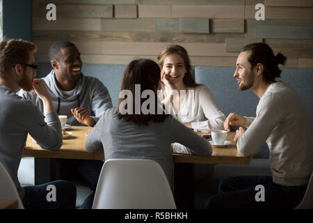 Multiethnic millennial friends sitting in cafe enjoying coffee laughing at jokes, diverse happy young people spend good time together having fun talki Stock Photo