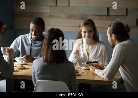 Happy diverse friends having fun in coffeeshop enjoying coffee and desserts, smiling multiethnic young people laughing at joke, spending great time to Stock Photo
