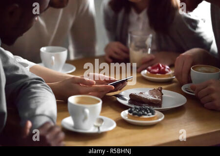 Close up of diverse friends sitting in coffeeshop watching picture on smartphone, multiethnic students have fun in cafe looking through photos on cell Stock Photo