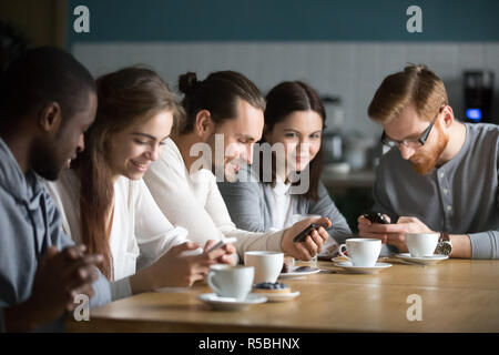 Diverse young people sit in cafe having fun using gadgets, multiethnic students spend time together in coffeeshop busy with smartphones, millennial co Stock Photo