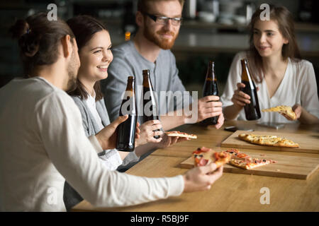 International students laugh having fun in Italian restaurant, diverse friends talk enjoying pizza and beer in cafe, millennial colleagues meet for lu Stock Photo