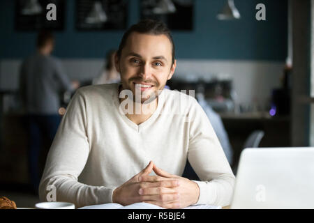 Portrait of smiling millennial man sitting in cafe with laptop and books on table, happy young guy work in coffeeshop using computer, male student loo Stock Photo