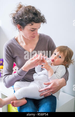 Mother giving her 16 month-old baby girl Doliprane ® with a pipette. Stock Photo