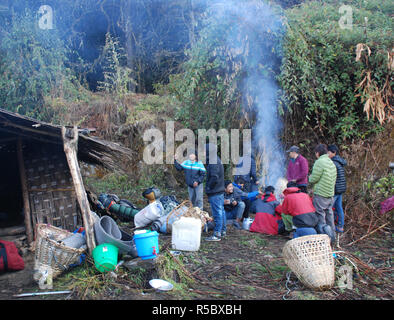 porters warm themselves around a fire next to a small shack in the forests of Eastern Nepal Stock Photo