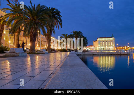 Waterfront of Split Croatia just after sunset. Lit buildings and palm trees, with reflection in water Stock Photo