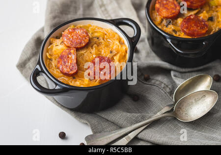 Slovak Christmas national cabbage soup in two small black pots with sausage on the tablecloth background. Stock Photo