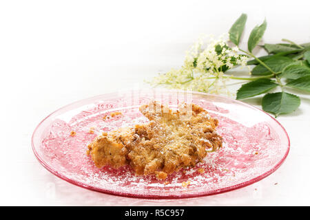 fried elderflower in pancake batter with powdered sugar on a pink glass plate, corner background fading to white, selected focus, narrow depth of fiel Stock Photo