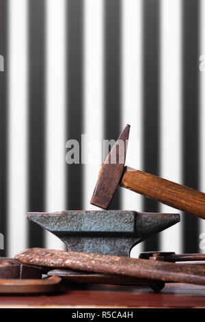 Old rusty rugged anvil, hammer and other blacksmith tools on striped black and white background. Stock Photo