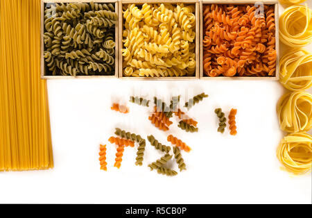 Three wooden boxes with colored fusilli are on a white background next to spaghetti and tagliatelle. isolated Stock Photo