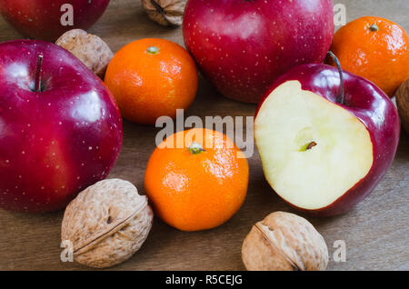 Organic whole and bitten off apples, tangerines and walnuts on a wooden background. Selective Focus. Rustic style. Stock Photo