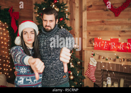 Merry Christmas and Happy New Year . Young couple celebrating holiday at home. Thumb down, new year, couple. Stock Photo