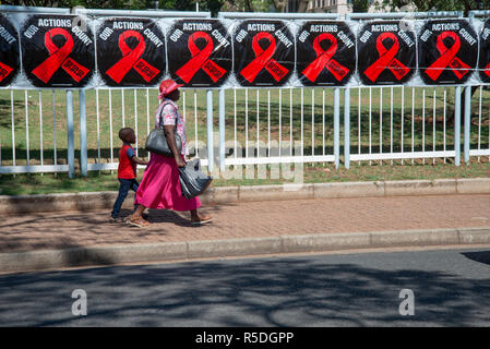 Johannesburg, South Africa, 1 December, 2018. A woman and child walk hand in hand past a row of World AIDS Day posters on Rosebank street. World AIDS Day is commemorated each year to create unity in the fight against HIV; show support for people living with HIV; and to remember those who have died from AIDS-related illnesses. South Africa is close to meeting first of the 90-90-90 UNAIDS targets, with 86 percent of people now aware of their status, says UNICEF. Eva-Lotta Jansson/Alamy Live News Stock Photo