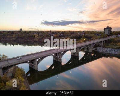 Aerial view of a bridge going over Saskatchewan River during a vibrant sunrise in the Fall Season. Taken in Saskatoon, SK, Canada. Stock Photo
