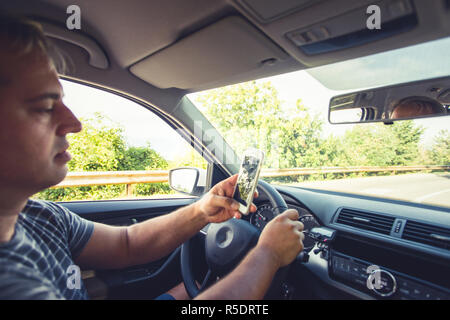 Young reckless man using his smartphone behind the wheel Stock Photo