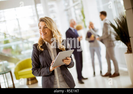 Portrait of young businesswoman using with tablet in office while other business people talking in background Stock Photo