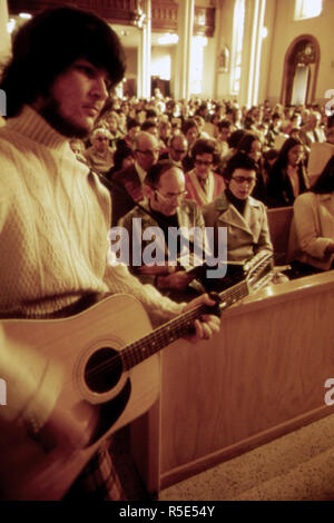 A Member of the New Ulm Cathedral Parish Is Shown Playing a Guitar at a Folk Mass. This Weekly Event Was Begun for the Young People and Has Become the Most Popular Mass with Standing Room Only. The Church Interior Is Decorated with Baroque Carvings Reminiscent of Churches in Southern Germany's Bavarian ca.1975 Stock Photo