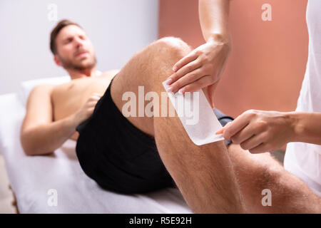 Therapist Hand Removing Hair On Man's Leg With Wax Strip Stock Photo